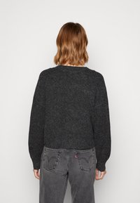 Ciemnoszary dziany sweter z okrągłym dekoltem, krótkim krojem i długimi, luźnymi rękawami, w połączeniu z wysokim stanem szarymi dżinsami.