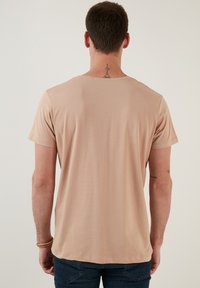Camiseta de manga corta y cuello redondo en un color beige claro, fabricada en algodón suave con una textura lisa. Presenta un diseño simple y sin patrones.