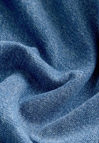 Denimska tkanina u različitim nijansama plave boje, koja prikazuje glatku teksturu s suptilnim uzorkom tkanja, drapirana u mekim nabiranjima.