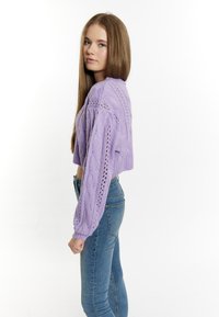 Gekürzter lila Kabelstrickpullover mit langen Ärmeln, der ein strukturiertes Muster und ein offenes Strickdesign aufweist, kombiniert mit eng anliegenden blauen Jeans.