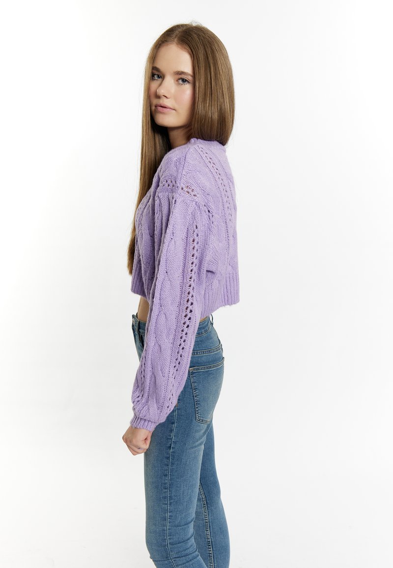 Gekürzter lila Kabelstrickpullover mit langen Ärmeln, der ein strukturiertes Muster und ein offenes Strickdesign aufweist, kombiniert mit eng anliegenden blauen Jeans.
