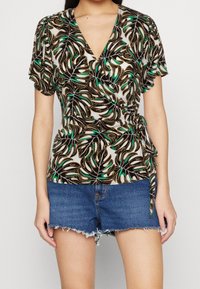 Top avvolgente con un motivo a foglia verde e nera su uno sfondo chiaro, con maniche corte e un nodo in vita. Abbinato a pantaloni corti di jeans.