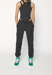 Svart ärmlös bodysuit med utskärningar, svarta joggingsbyxor med dragsko och gröna högtoppskor med vita accenter.