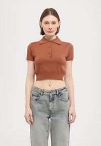Brun cropped polo skjorte med krage, korte ermer og tre knapper. Kombinert med høyt liv lyseblå jeans. Minimalistisk design.