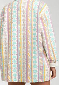 Patterned oversized shirt featuring vertical stripes in pastel colors, with floral and geometric designs. Soft, textured fabric.