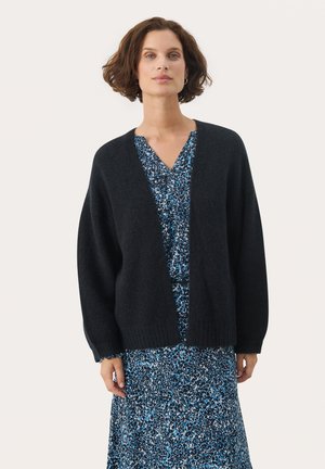 Black oversized cardigan with a V-neck design, ribbed hem, and dropped shoulders, worn over a blue patterned dress. Soft texture.