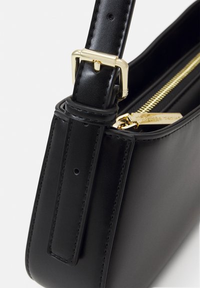 Angolo di una borsa in pelle nera con fibbia dorata e tirazip, che mostra la tracolla e la cucitura dettagliata.