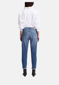 Jeans in denim azzurro chiaro con taglio dritto, orli arrotolati e tasche posteriori visibili, abbinati a una camicia bianca con colletto e bottoni.
