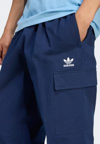 Navy blue cargo pants made of textured fabric, featuring a front patch pocket and white Adidas logo on the thigh.