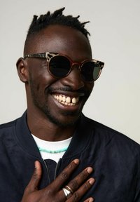 Lunettes de soleil avec des verres ronds noirs et un motif écaille de tortue marron. Elles présentent une monture épaisse avec un mélange de sections unies et à motifs.