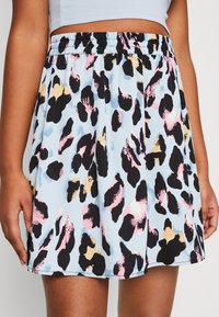 Kvinna som bär en ljusblå kjol med svarta, rosa och beige leopardmönster och ett elastiskt midjeband, kombinerat med en kortärmad ljusblå topp.