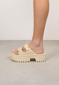 Sandali platform beige con doppie fibbie regolabili, suola spessa e testurizzata, design aperto e punta arrotondata, che mette in mostra una superficie liscia.