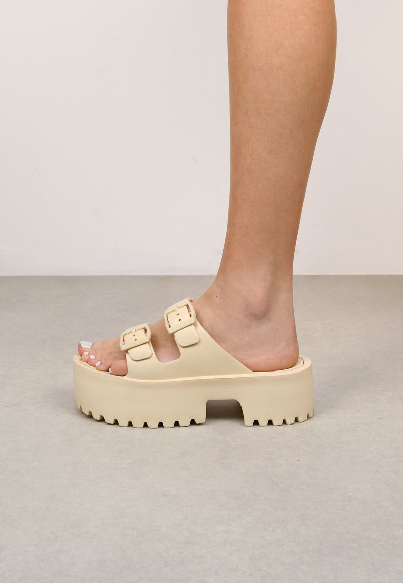 Sandali platform beige con doppie fibbie regolabili, suola spessa e testurizzata, design aperto e punta arrotondata, che mette in mostra una superficie liscia.