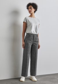 Harmaa lyhythihainen paita, jossa on sileä pinta, yhdistettynä korkeavyötäröisiin musta-valkoisiin ruutukuvioisiin leveälahkeisiin housuihin. Valkoiset tennarit viimeistelevät asun.