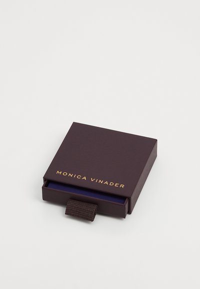 Caixa roxa escura com um logotipo dourado, apresentando uma aba de puxar, revestida com um tecido interior azul, formato quadrado, textura suave.