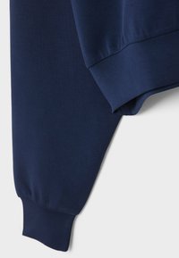 Manche de sweat-shirt bleu marine avec bord-côte, montrant la texture du tissu et les détails de couture sur fond blanc.