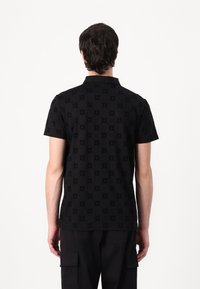 Svart polo-skjorte med teksturert mønster, korte ermer og krage, med et subtilt gjentatt design over stoffet.