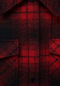 Rød og sort ternet skjortejakke lavet af uldblandingsstof. Har store sorte knapper og to frontlommer. Blød tekstur, flannel finish.