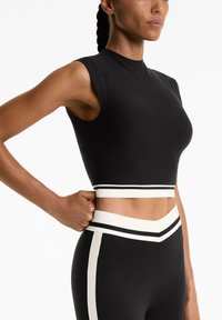Crni atletski crop top s kratkim rukavima, koji ima prilagođeni dizajn i bijelu prugastu traku oko struka, glatku teksturu i minimalne šavove.