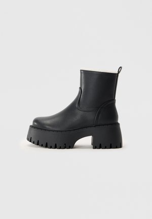 Black ankle boots made of smooth leather with a thick, ridged rubber sole. Features a rounded toe and a fabric lining at the top edge.