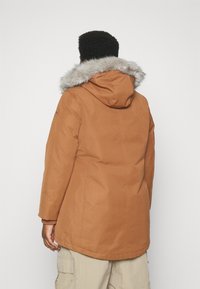 Chaqueta parka marrón con capucha de pelo, con una textura suave y bolsillos laterales, vista desde la espalda.