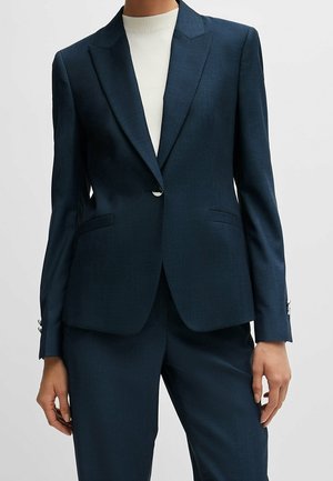 Marineblå skræddersyet blazer med enkelt knap og matchende bukser båret over hvid ribbet højhalset top.