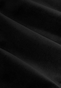 Zwarte fluwelen stof met een gladde textuur, met zachte, vloeiende plooien die een gevoel van diepte en rijkdom in het uiterlijk creëren.