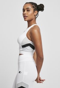 Top court blanc à motifs chevrons gris et noir, associé à un legging blanc taille haute avec un logo accentué près de la hanche.