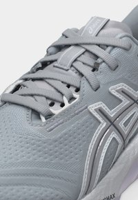 Κοντινό πλάνο ανοιχτό γκρι παπουτσιού τρεξίματος Asics με υφασμάτινο δίχτυ, δεμένα κορδόνια και διακριτικό λογότυπο στο πλάι και στη γλώσσα.