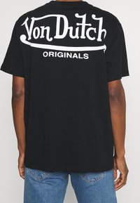 Camiseta negra con el texto blanco "Von Dutch ORIGINALS" en la parte posterior, corte estándar, mangas cortas y material de algodón suave.