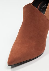 Stivale alla caviglia in suede marrone con punta affusolata e pannello laterale testurizzato. Finitura liscia e design elegante per un aspetto snello.