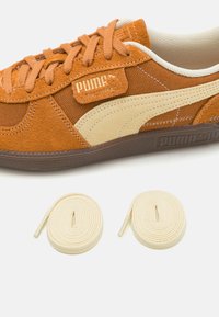Puma suede tennarit oranssina ja kermanvärisenä, jossa on teksturoitu päällinen, litteät nauhat ja kontrastivärinen ruskea pohja. Mukana kaksi lisäkermanväristä nauhaa.