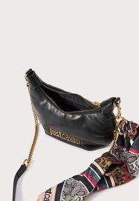 Sac en cuir noir avec quincaillerie dorée, fermeture éclair et logo en relief. Comprend une écharpe en soie à motif attachée à la sangle.