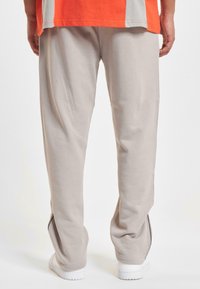 Lys grå joggebukser med smale ben, elastisk midje og sidelommer med glidelås. Mykt bomullsmateriale, kombinert med hvite joggesko.