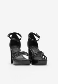 Sandalias de tacón alto negras con diseño de punta abierta, que cuentan con múltiples correas en la parte frontal y una correa en el tobillo, fabricadas en cuero suave.