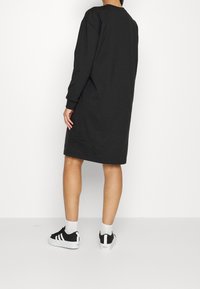 Svart oversized sweatshirtklänning med långa ärmar, ribbade muddärmar, rund halsringning och en slät yta, i kombination med svarta och vita sneakers.