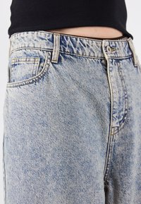 Jeans in denim azzurro chiaro con vita alta, dotati di tasche standard, cuciture a contrasto e una vestibilità rilassata. Nessun motivo visibile.