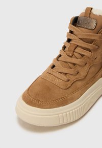Zapatillas de ante marrón con un acabado texturizado, punta redonda y suela de goma color crema. Presenta detalles cosidos y cierre con cordones.