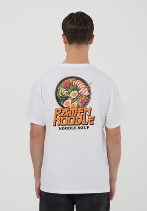 T-shirt bianco in cotone con una grafica colorata di ramen sulla schiena, che include uova, gamberi e verdure, accompagnata da testo in grassetto.
