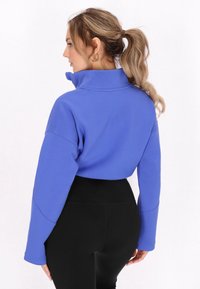 Kratttad sweatshirt i livlig blå färg, med hög krage och långa ärmar, tillsammans med högmidjade svarta leggings. Slät textur.