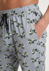 Grijze shorts met een herhalend patroon van groene en zwarte dierengezichten, voorzien van een elastische tailleband en zijzak.