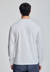 Langsleeve shirt van witte katoen, met een eenvoudige ronde halslijn en een gladde textuur. Zichtbare stiksels langs de zoom en mouwen.