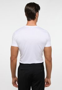 Witte korte mouwen t-shirt met een ronde hals, gedragen met zwarte broek met achterzakken en knoopaccenten.