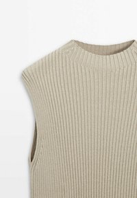 Beżowy, prążkowany top bez rękawów z wysokim dekoltem i bocznymi rozcięciami, wykonany z teksturowanej dzianiny. Proste, minimalistyczne elementy wzornictwa.
