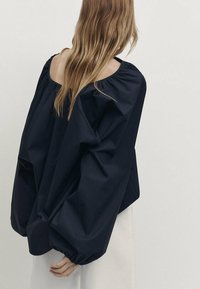 Marinblå oversized blus i lättviktsmaterial. Har stora puffärmar och en vid halsringning, med en slät, matt yta.