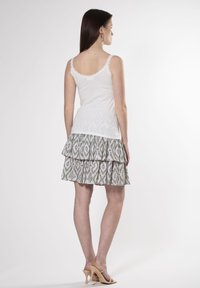 Top bianco senza maniche con pizzo, abbinato a una gonna a strati con motivo in tonalità verde e rosa. Indossato con sandali con tacco beige.