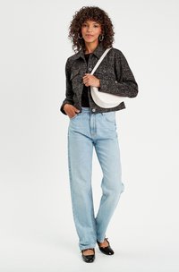 Giacca cropped nera con texture, top nero, jeans skinny blu chiaro, ballerine nere e borsa a tracolla bianca; modella con capelli ricci.