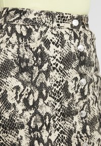 Jupe en denim à imprimé serpent noir et beige, avec une taille haute, une fermeture à boutons sur le devant et une légère texture.