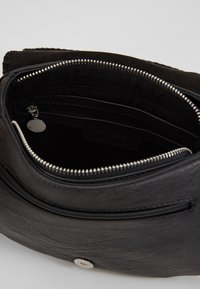 Interiér černé kožené tašky obsahuje více přihrádek, hladkou texturu, kapsu na zip a stříbrné kovové doplňky.