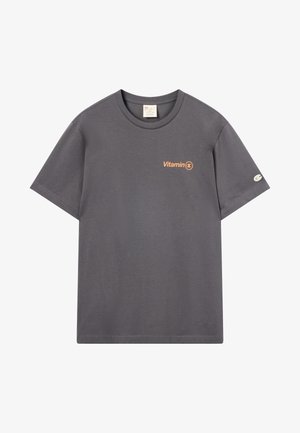 Donkergrijze t-shirt met korte mouwen met oranje "Vitamin C" tekst op de borst en een klein wit logo op de linkermouw.